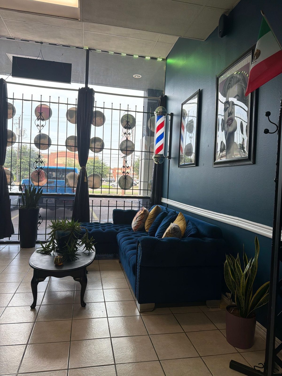 Zona de espera con sofá azul de terciopelo, plantas y barber pole en la ventana